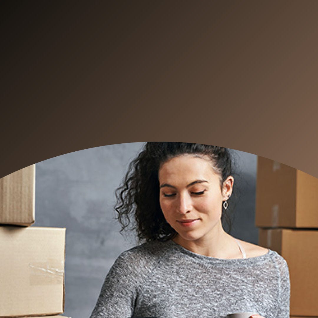 Small business owner surrounded by shipping boxes paying with phone. 