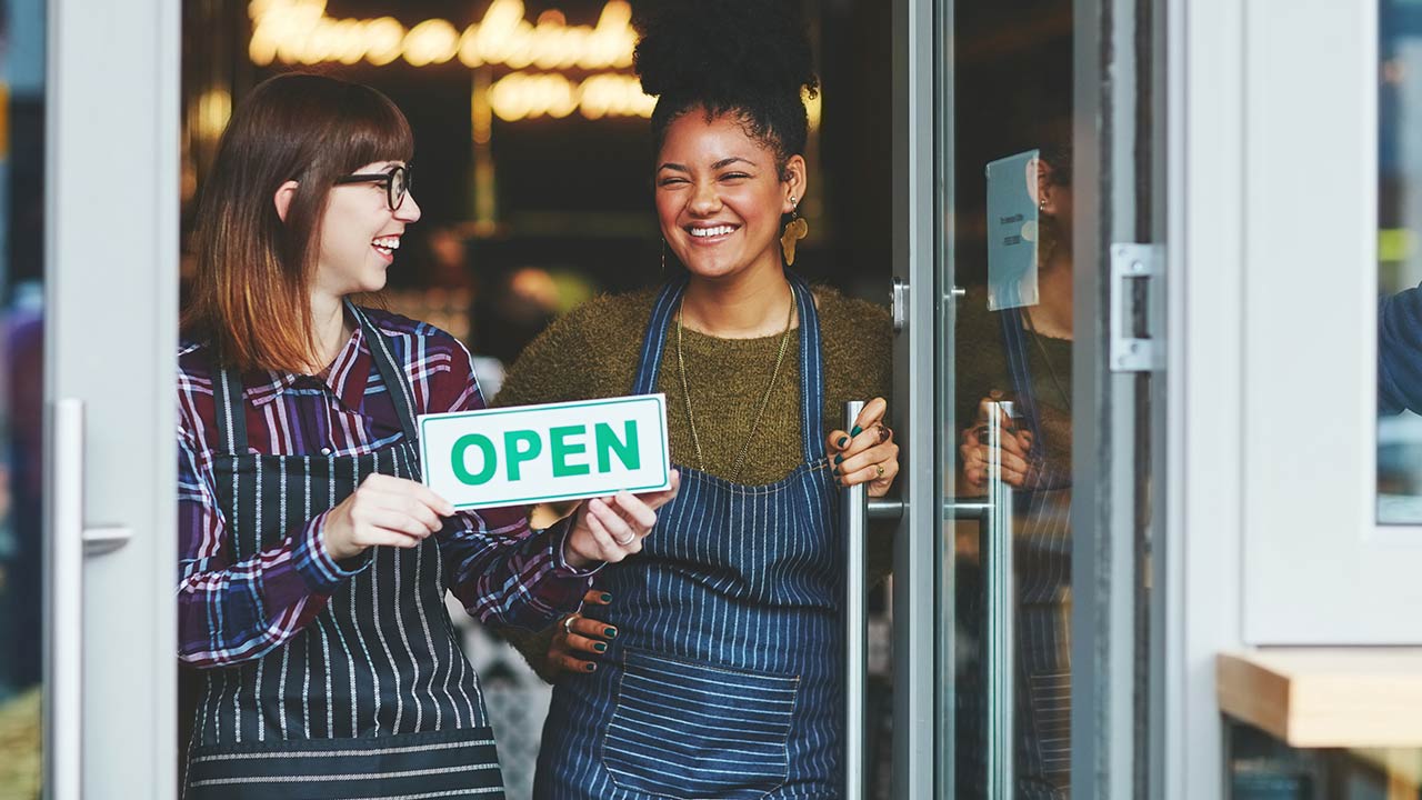 Two young women holding up open sign coffee shop.