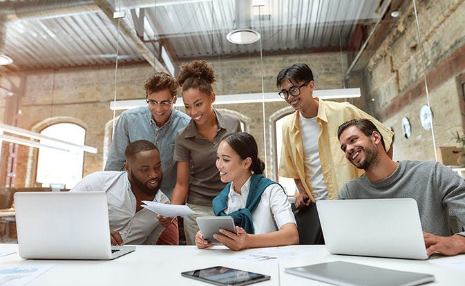 A diverse group of people seated around a table, each using laptops for a collaborative work session.
