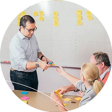 Man handing sticky notes to two colleagues at a table in a meeting room.